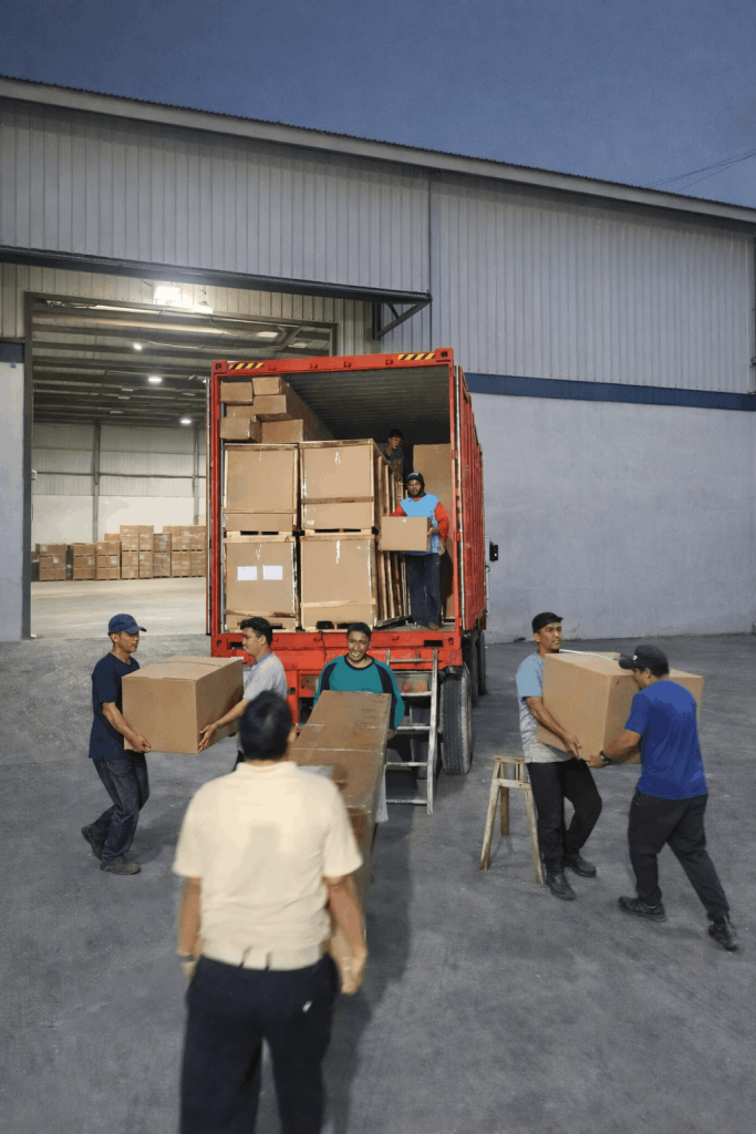 Workers loading packed furniture boxes into a shipping container at a woodworking warehouse